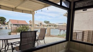 A covered patio area with a table and chairs, a view of a residential neighborhood, and a gated swimming pool. - Minimalist Lake House (Helendale)