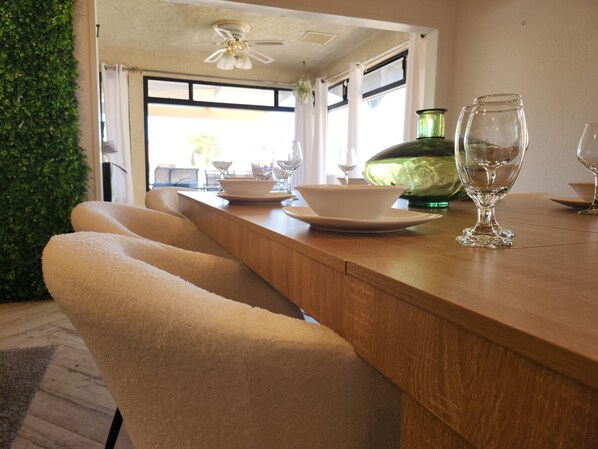 Een eetgedeelte met een houten tafel, witte stoelen en een groene vaas.