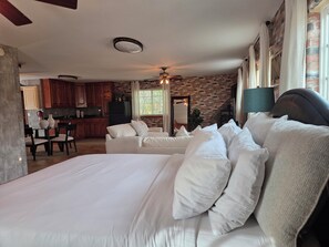 Une chambre avec un grand lit, un coin repas avec une table et des chaises, et une cuisine avec des meubles en bois et un mur en briques.