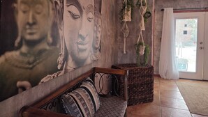 Ein Zimmer mit einer großen Buddha-Muralmalerei, einer Holzbank mit gemusterten Kissen, Wandteppichen aus Makramee und einem Korbwäscheschrank.