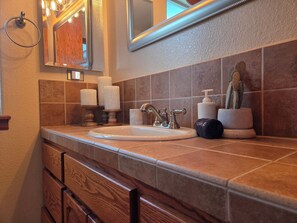 A bathroom with a sink, mirror, towel rack, candles, and a potted plant. - Zen Den Studio (Apple Valley)