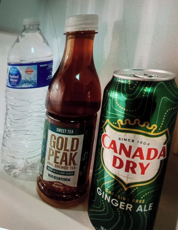 Une étagère avec une bouteille de thé glacé Gold Peak, une bouteille de ginger ale Canada Dry et une bouteille d’eau purifiée.