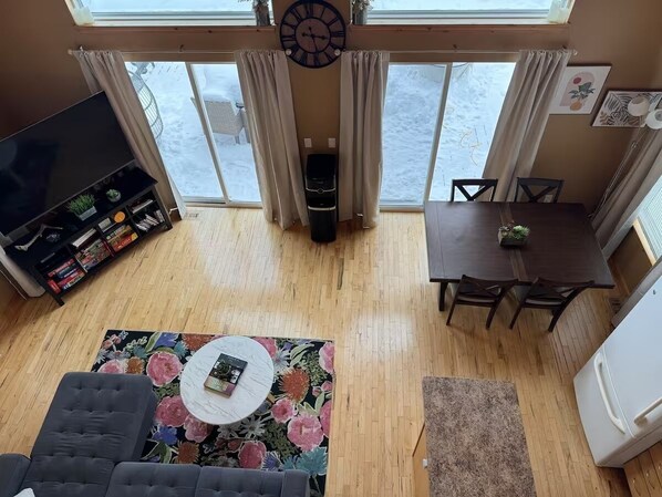 Un salon comprenant un téléviseur, une bibliothèque, un tapis à motifs floraux et un coin repas avec une table et des chaises.