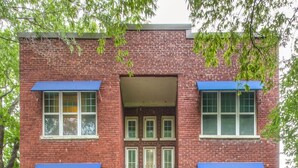 A red brick building with a central entrance, multiple windows, and blue awnings. - Carson Flats Apt #4 | 1BR • Near BOK• OSU Med•Dtwn (Tulsa)