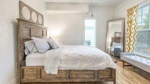 A bedroom with a wooden bed, a ceiling fan, a window with blinds, and a mirror. - Carson Flats Apt #4 | 1BR • Near BOK• OSU Med•Dtwn (Tulsa)