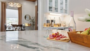 Un plan de travail en marbre avec deux verres de vin blanc, une bouteille et un bol rempli de fruits et de fromage.