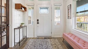 Un couloir avec une porte blanche, un banc et une petite table sur laquelle est posée une plante.