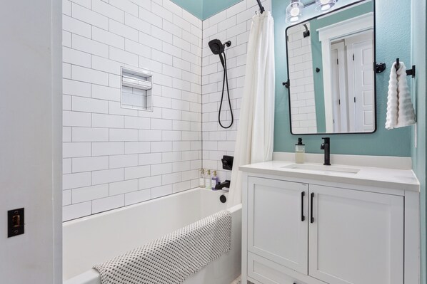 A bathroom with white subway tiles, a white bathtub, a white vanity with black handles, and a mirror with a white towel hanging on the wall.