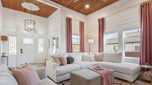 Un salon spacieux avec un grand canapé blanc, un pouf beige et un tapis à motifs.