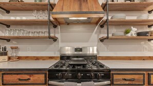 A kitchen with a central stove, wooden shelves above, and drawers below. - Rustic Charm Owasso Retreat | 2BR • Big Backyard (Owasso)