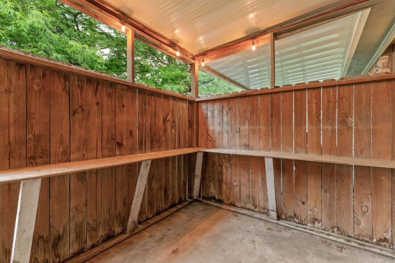 Een houten kamer met een schuine kap, inbouwplanken en een raam met uitzicht op groen.