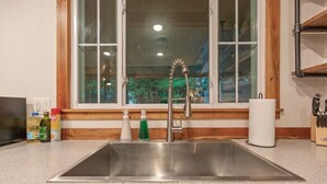 A kitchen with a stainless steel sink, wooden countertop, and a window with a view of trees. - Rustic Charm Owasso Retreat | 2BR • Big Backyard (Owasso)