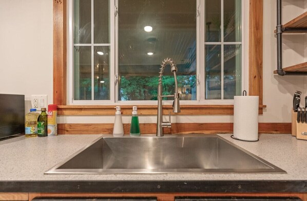 A kitchen with a stainless steel sink, wooden countertop, and a window with a view of trees. - Rustic Charm 2BR · Fenced Yard · Pets OK · Owasso (Owasso)