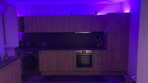 A compact kitchen with wooden cabinets, a built-in oven, and a washing machine. - Le Bastion, l'appartement au pied de la Citadelle (Bitche)