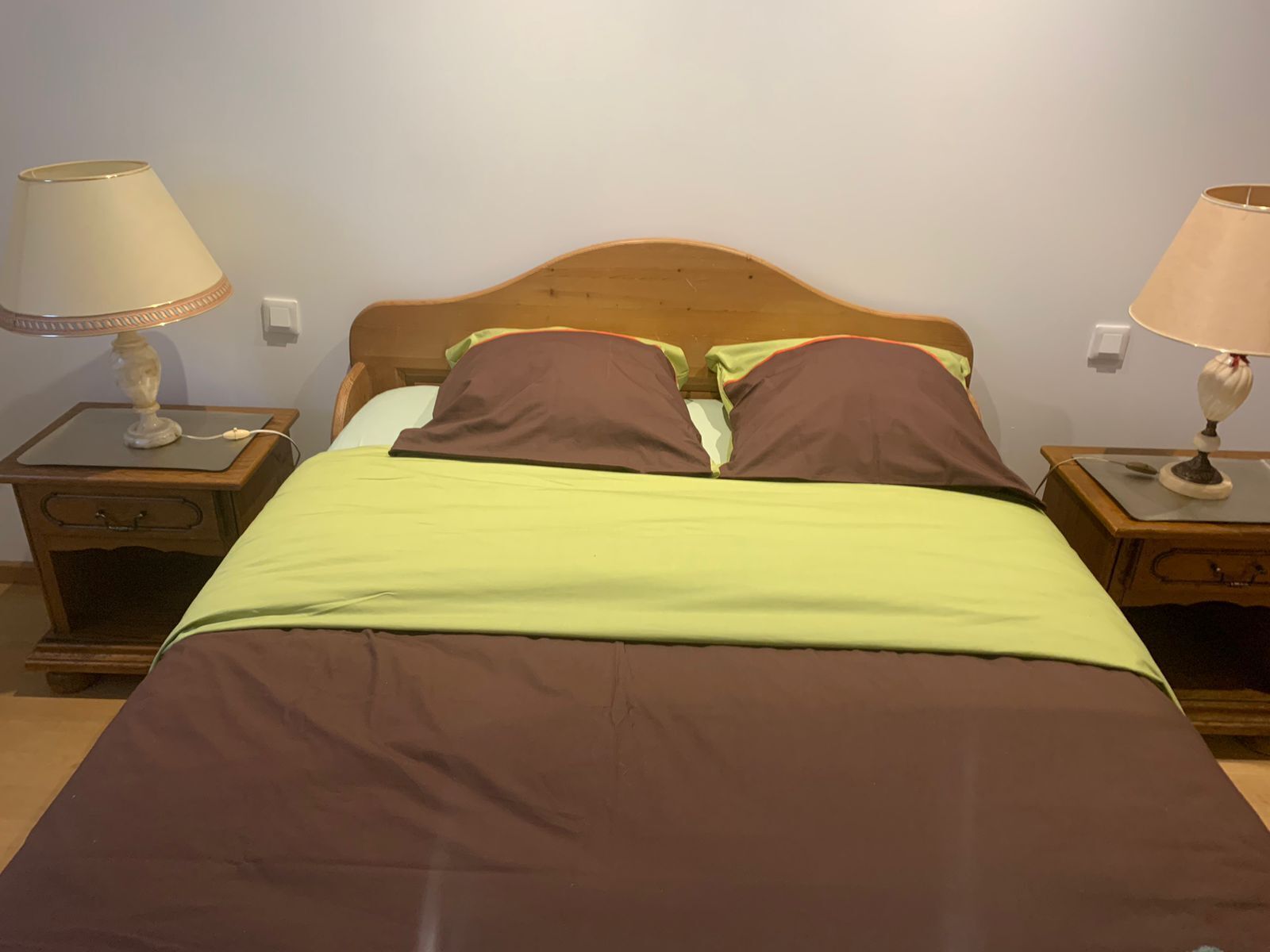 A single bed with a wooden headboard, two bedside tables with lamps, and a green and brown bedspread.