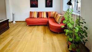A spacious living room with a red sectional sofa, two framed artworks on the wall, a large window with a view, and a potted plant. - Le Bastion, l'appartement au pied de la Citadelle (Bitche)