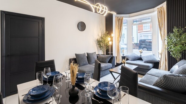 A modern dining area with a black and white color scheme, featuring a dining table set with blue plates and glasses, a black vase with dried flowers, and a contemporary light fixture. - Open Mind Property - 7 Beds and Free Parking (Portsmouth)