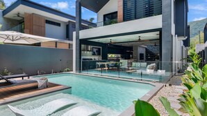 A modern house with a swimming pool, outdoor seating, and a glass-enclosed kitchen.