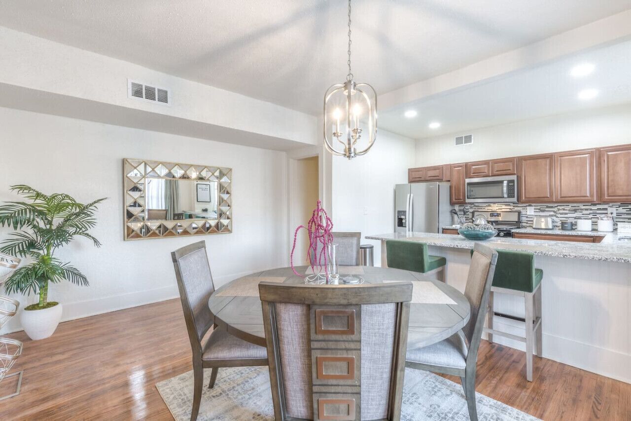A modern kitchen with wooden cabinets, a central island, and a dining area with a round table and chairs.