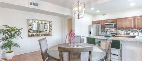 A modern kitchen with wooden cabinets, a central island, and a dining area with a round table and chairs.