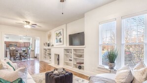 A spacious living room with a large TV, a fireplace, and a dining area visible through an open door. - Carson Flats Apt #2 | 1BR • Near BOK• OSU Med•Dtwn (Tulsa)