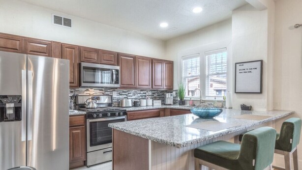 A modern kitchen with stainless steel appliances, wooden cabinets, and a granite countertop. - Carson Flats Apt #2 | 1BR • Near BOK• OSU Med•Dtwn (Tulsa)