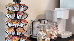 Una estación de café con una cafetera, un soporte para tazas y un tarro de cápsulas de café.