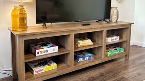 Un mueble de madera para entretenimiento con un televisor de pantalla plana, una lámpara y estantes con juegos de mesa.