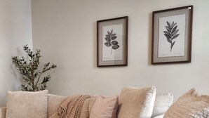Un salón con un sofá seccional color beige, una mesa de centro y dos láminas botánicas enmarcadas en la pared.
