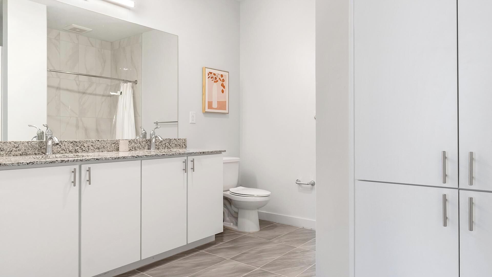 A modern bathroom with a large mirror, a shower, a toilet, and a cabinet with a towel rack.