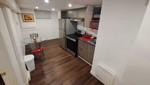 Une cuisine compacte équipée d’un réfrigérateur, d’une cuisinière, d’un four à micro-ondes et d’un petit coin repas avec une table en verre et des chaises rouges.