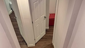 Un escalier recouvert d’une moquette rouge mène à une pièce dont la porte est blanche et qui contient un pouf rouge.