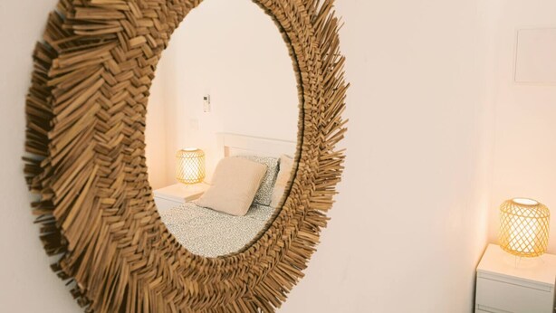 Une chambre comprenant un lit, une table de chevet et un miroir mural avec un cadre tressé.