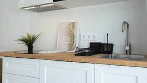 Une cuisine moderne avec des meubles blancs, un plan de travail en bois, un micro-ondes noir, un évier en acier inoxydable et une plante en pot.