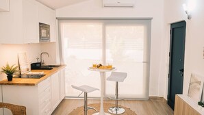 Une cuisine compacte avec des meubles blancs, un évier et un petit coin repas équipé de deux tabourets.