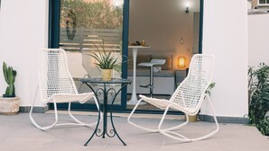 Une terrasse avec deux chaises en osier blanc, une petite table ronde et un pot de fleurs.