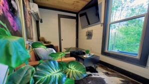 A modern living room with a large window, a flat-screen TV, and a cowhide rug. - Lion Den Cabin A at Walterfalls-Upstate SC (Six Mile)