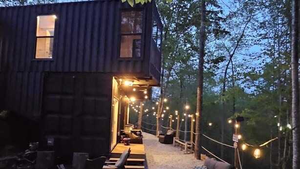 A rustic cabin with a porch, string lights, outdoor seating, and a forest backdrop. - Lion Den Cabin A at Walterfalls-Upstate SC (Six Mile)