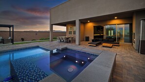 A modern outdoor pool area with a hot tub, seating, and a patio with a view of the mountains.