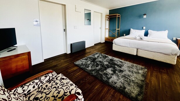A modern hotel room with a large bed, a TV on a wooden dresser, a wardrobe, and a mirror. - Bings Motel (Blenheim)