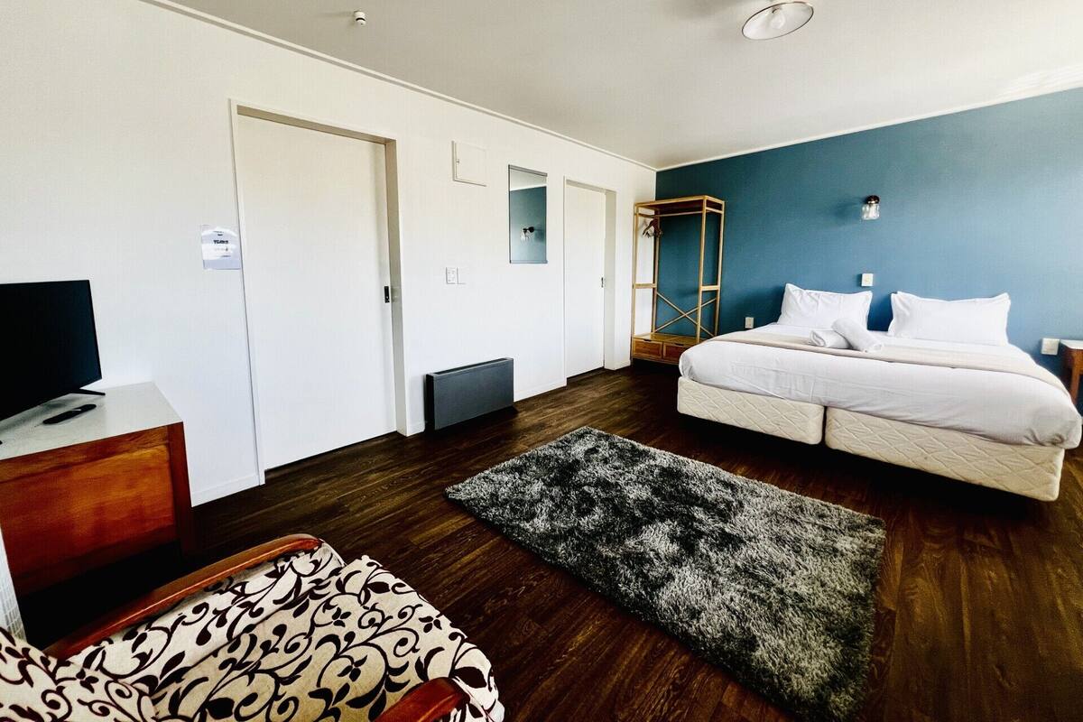 A modern hotel room with a large bed, a TV on a wooden dresser, a wardrobe, and a mirror.