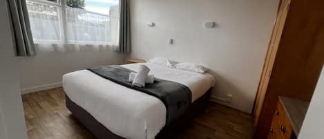A bedroom with a bed, wooden flooring, a window with curtains, and a wooden wardrobe.
