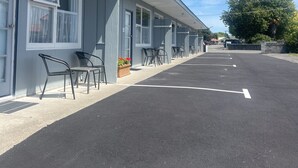 A motel with a row of rooms, each with a window and a door. There are outdoor chairs and a small planter with flowers. - Bings Motel (Blenheim)