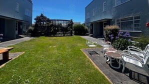 A courtyard with a lawn, a metal fence, and outdoor seating. - Bings Motel (Blenheim)