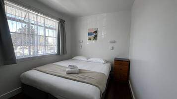 A bedroom with a bed, a nightstand, a window with curtains, and a wall-mounted picture.