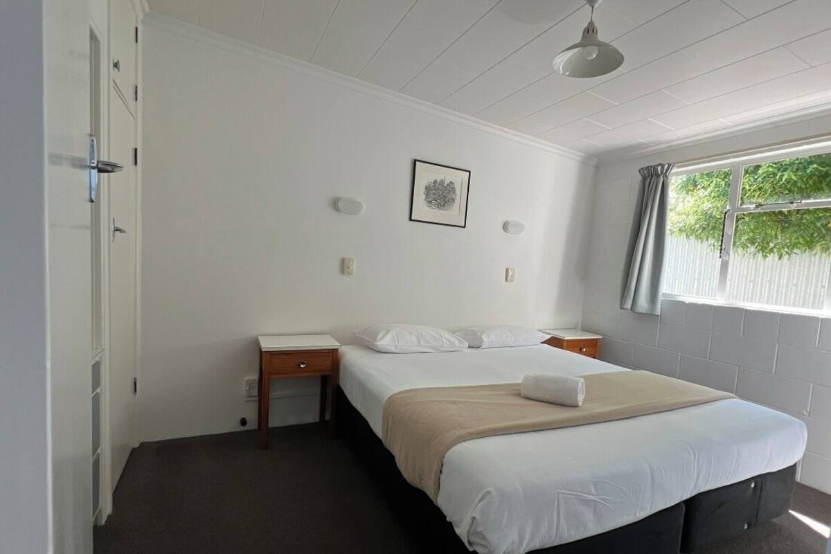A bedroom with a bed, bedside tables, a desk, a chair, a window with curtains, and a ceiling light.