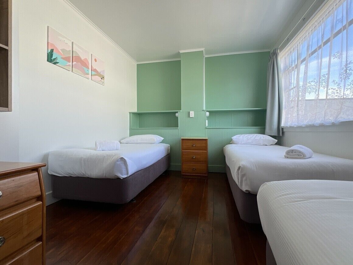 A room with two beds, a wooden dresser, and a window with curtains.