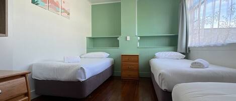 A room with two beds, a wooden dresser, and a window with curtains.