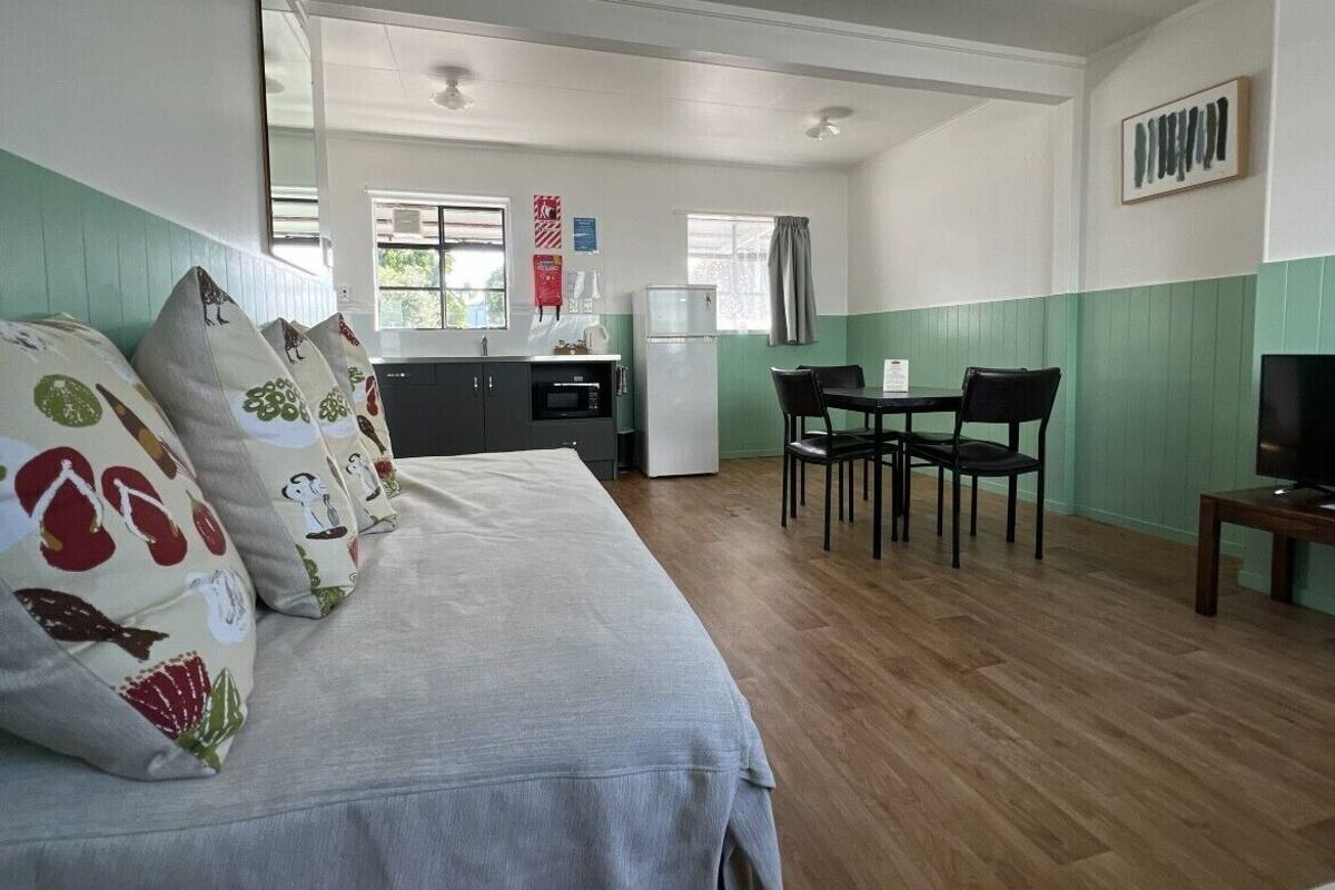 A room with a bed, a dining table with chairs, a television, and a kitchen area with a refrigerator.