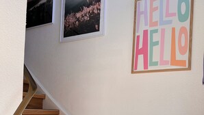 Una escalera de madera con barandilla blanca, un cartel con la palabra 'HELLO' y dos cuadros en la pared.